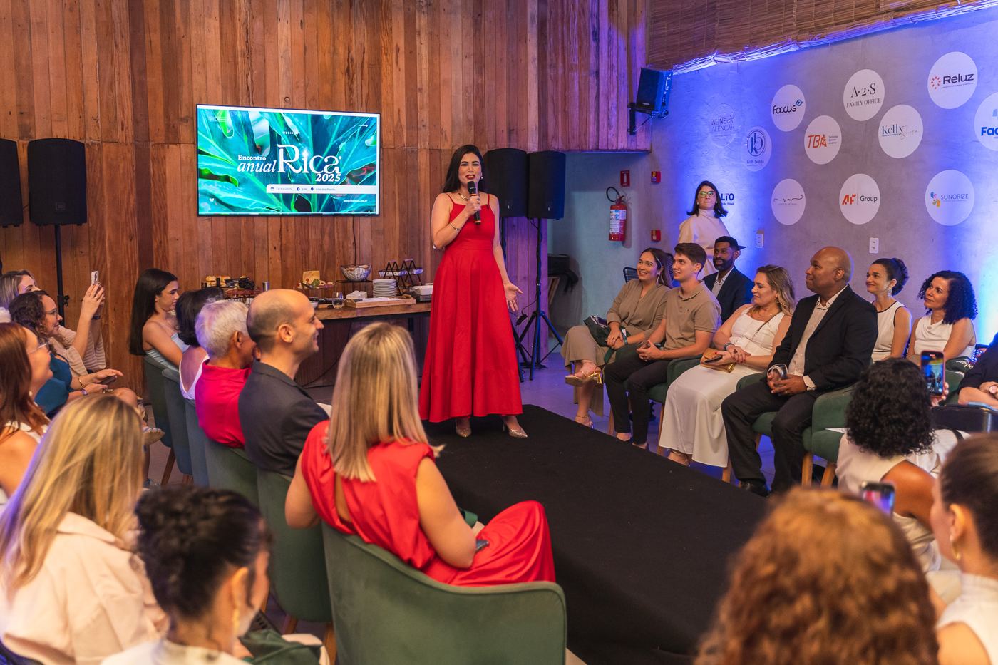 Aline Alencar, de vestido vermelho, fala à plateia no Encontro Anual RICA 2025.