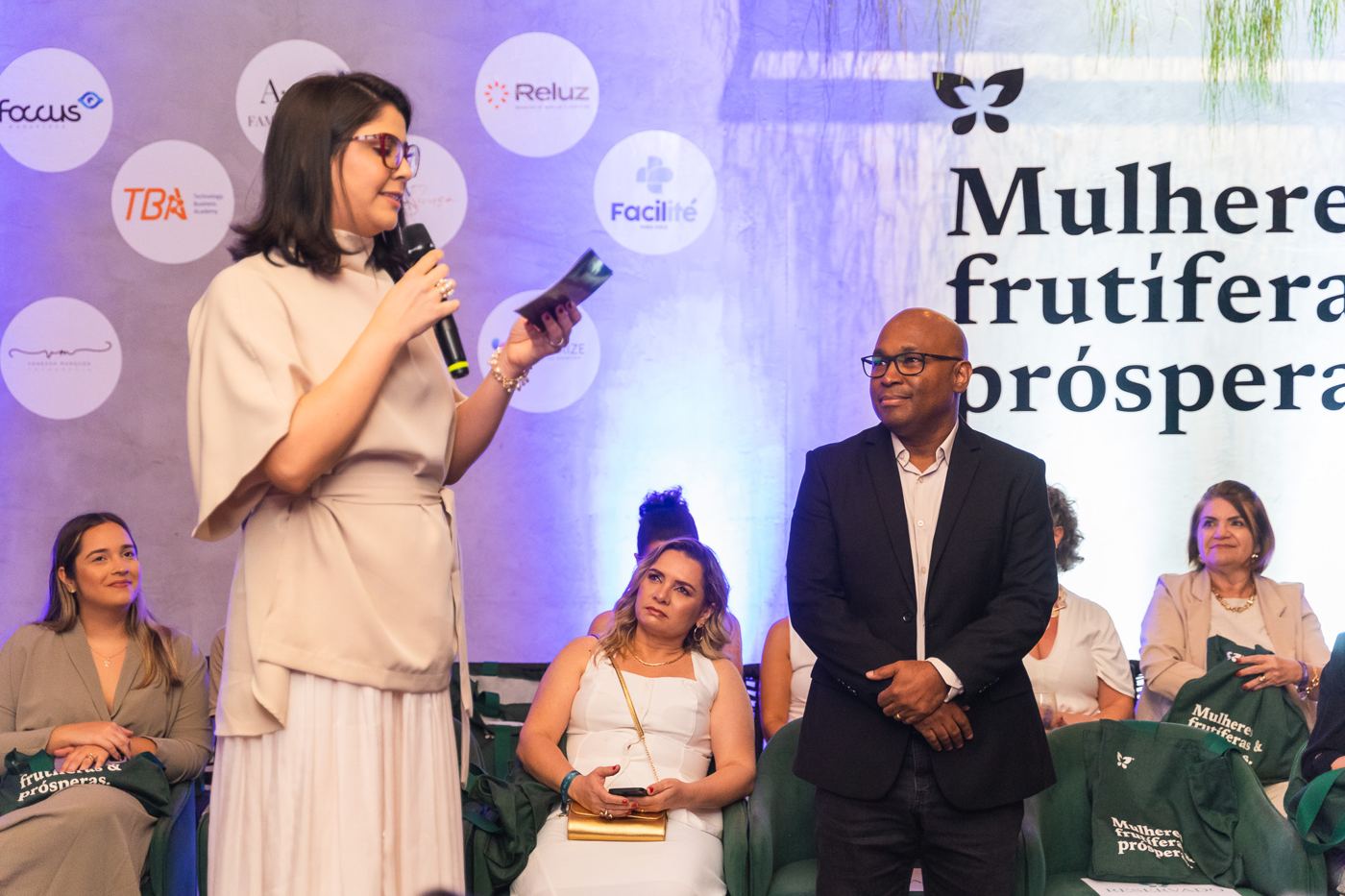 Participante fala ao microfone diante da plateia e do painel Mulheres frutíferas e prósperas.